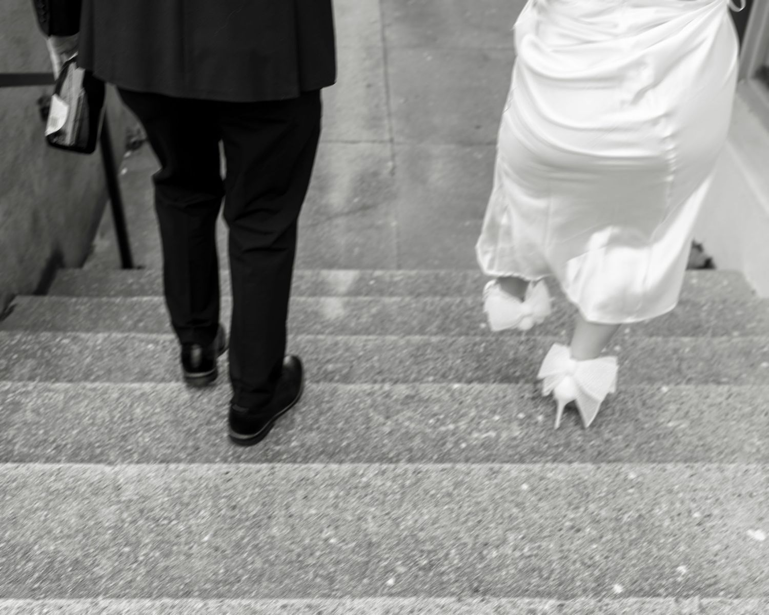 Black and white photo of bride and groom ascending stone steps, bride wearing white heels and gown.