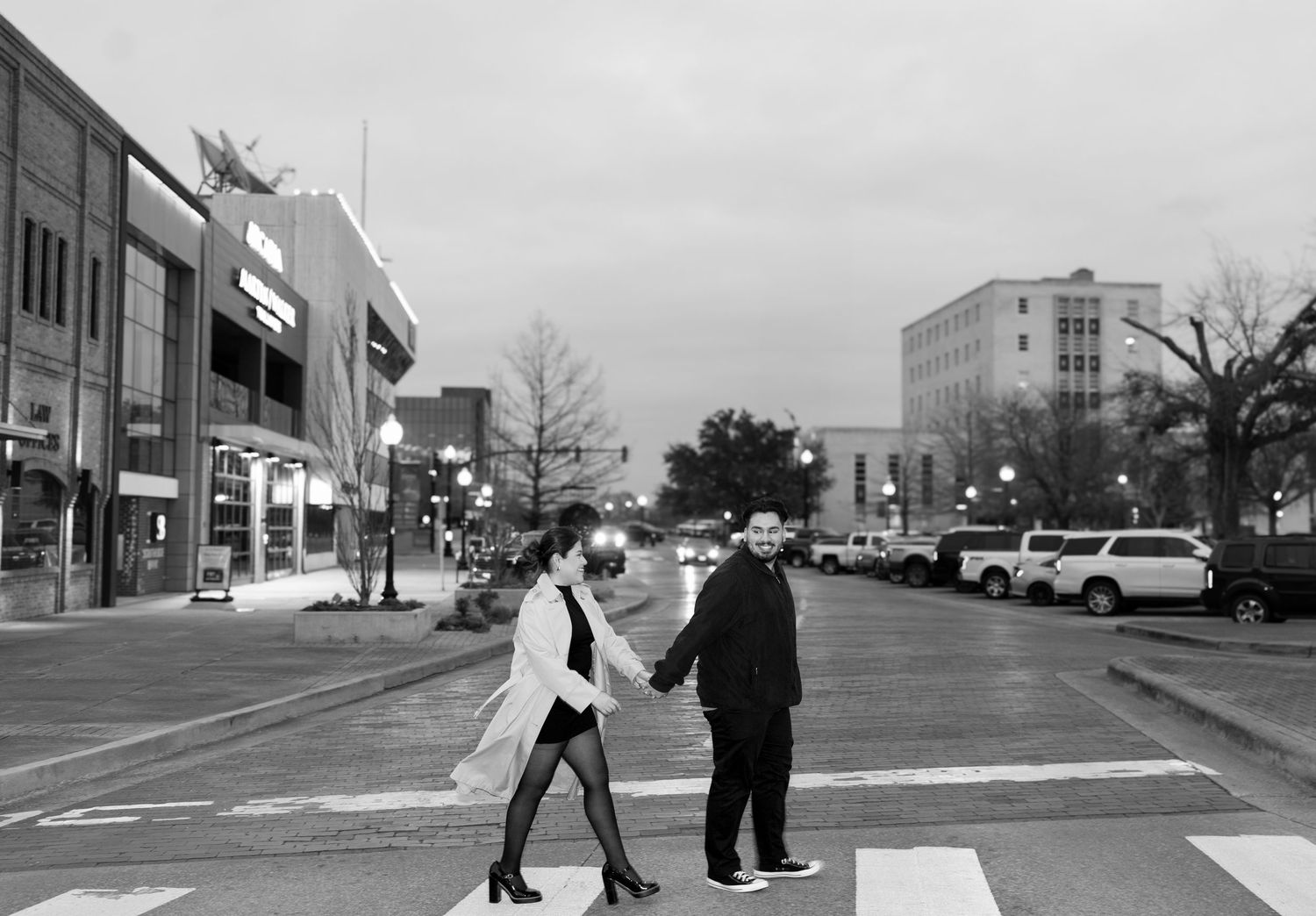 Black and white photo of a couple holding hands while crossing a street in a downtown urban area.