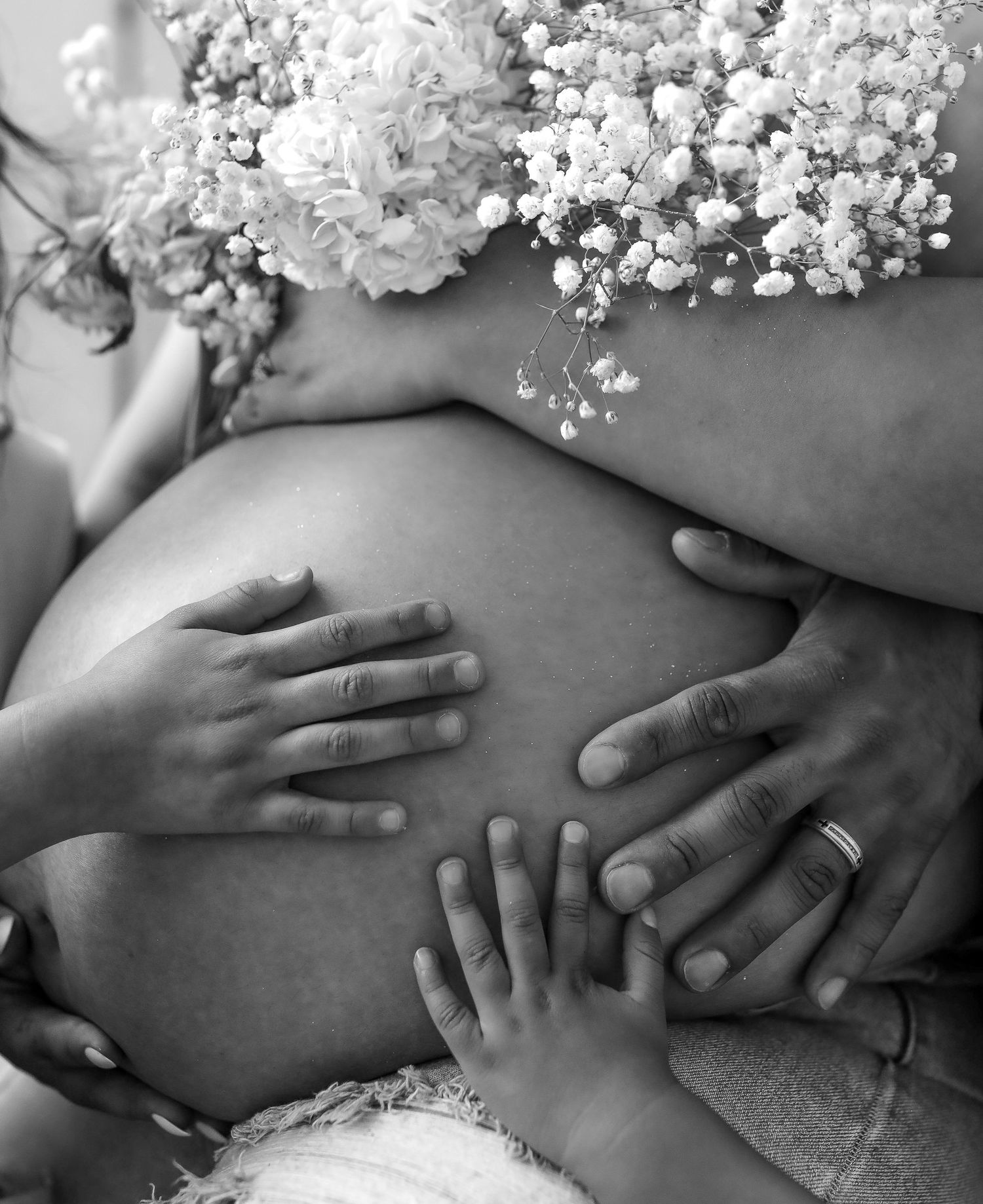 Black and white photo of hands cradling a pregnant belly adorned with white flowers.