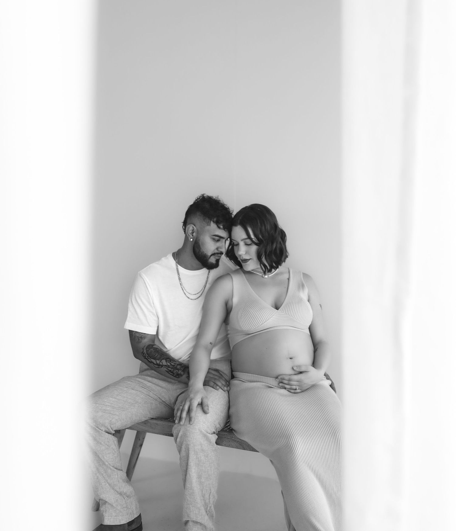 Couple sharing tender moment during maternity photo session, black and white studio portrait.
