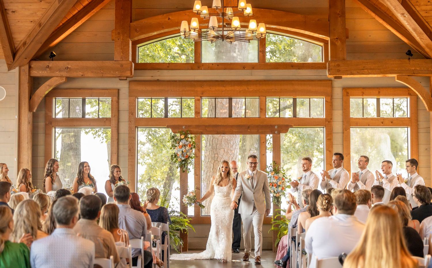 Bride and groom walk back down the aisle as guests celebrate inside a beautiful timber-frame wedding venue.