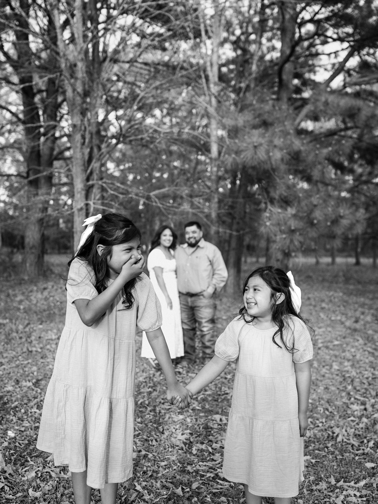 Two girls in white dresses laughing with parents in background.