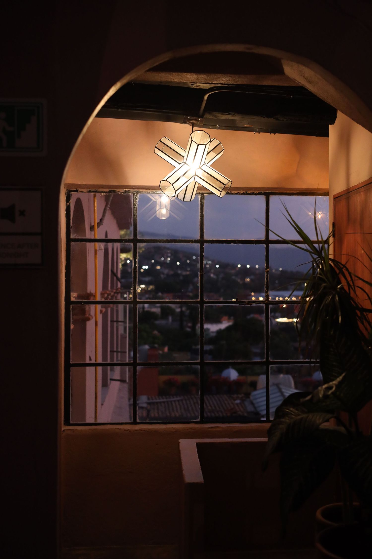Cozy interior view through arched doorway with star-shaped pendant light illuminating a grid window overlooking city lights at night.