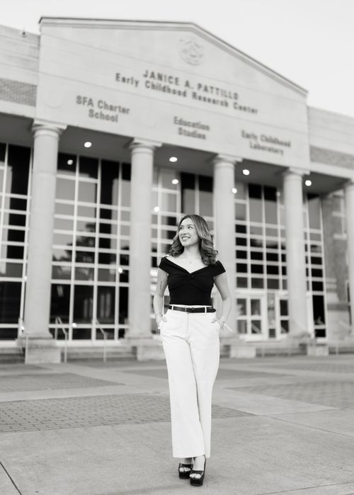 Black and white photo of smiling woman in white pants outside Janice A. Pattillo Early Childhood Center.
