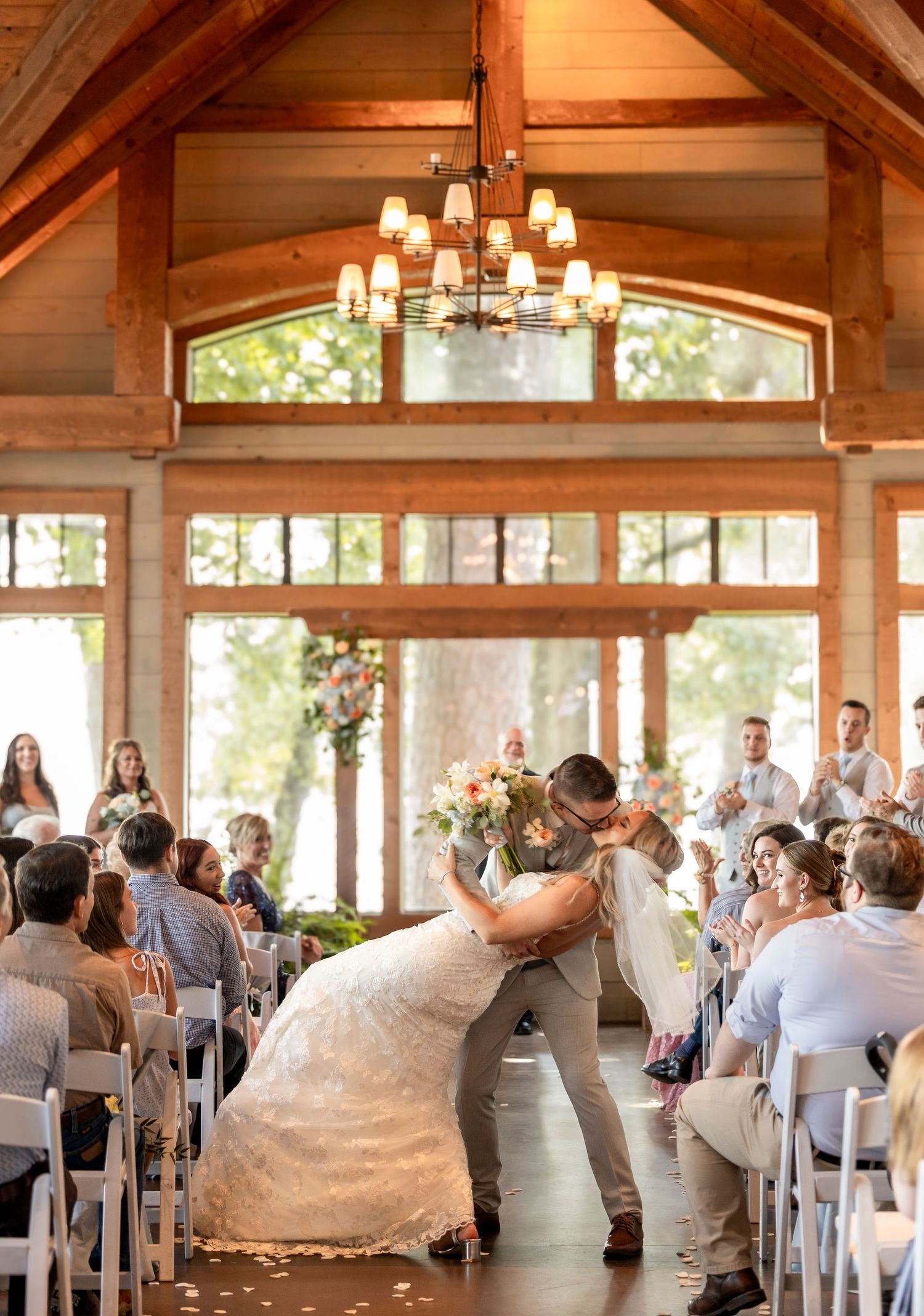 Groom dips bride for a kiss at the altar inside a stunning rustic wood chapel as guests cheer.
