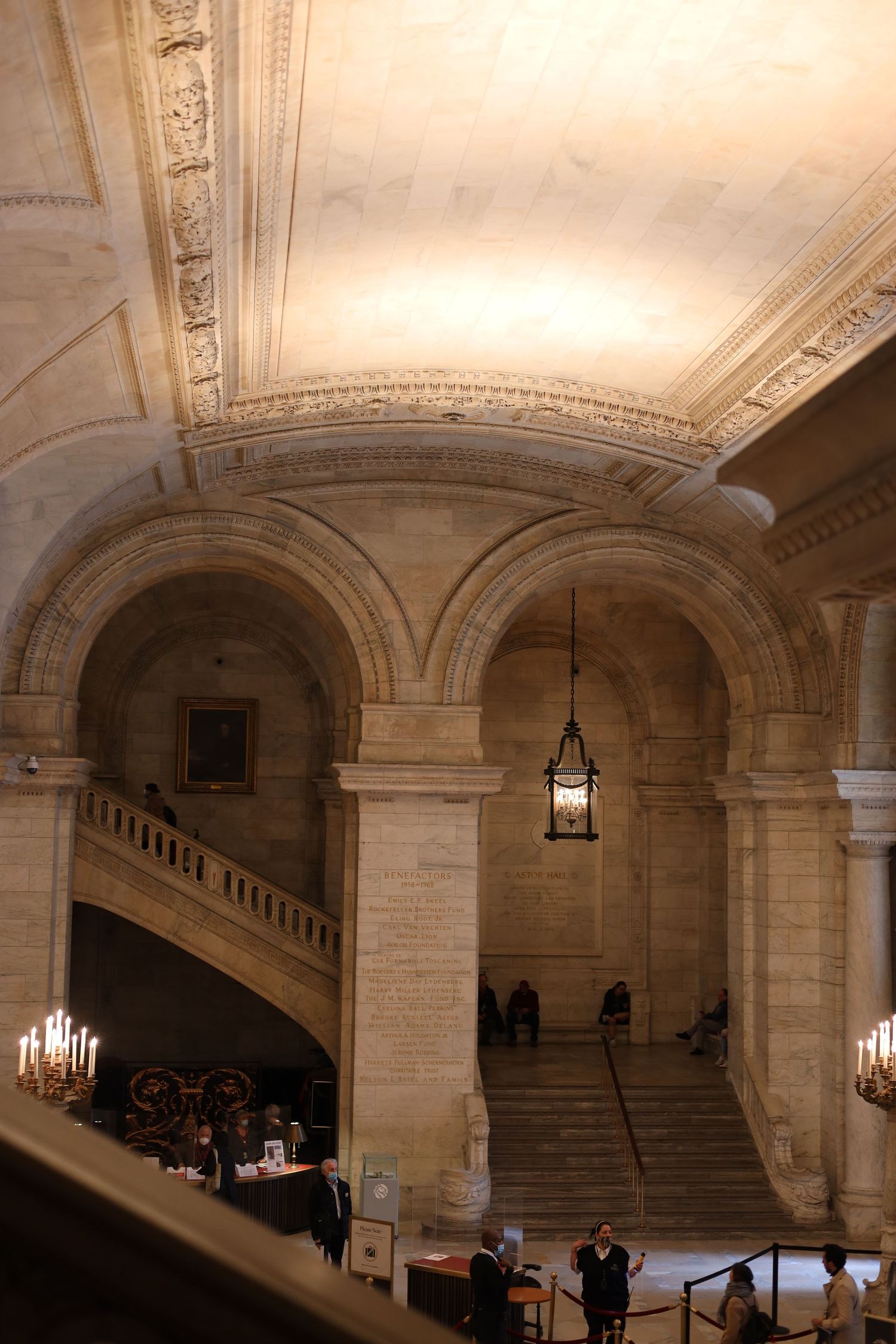 Grand interior of a historic library featuring arched stone columns, ornate ceiling, hanging lantern, and marble staircases.