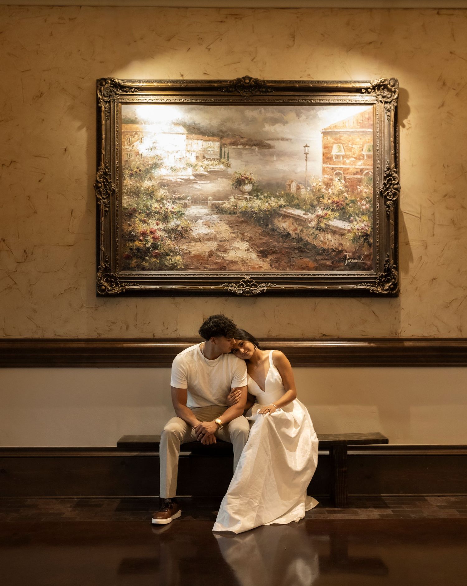 Couple sitting closely beneath an ornate painting in an elegant interior.