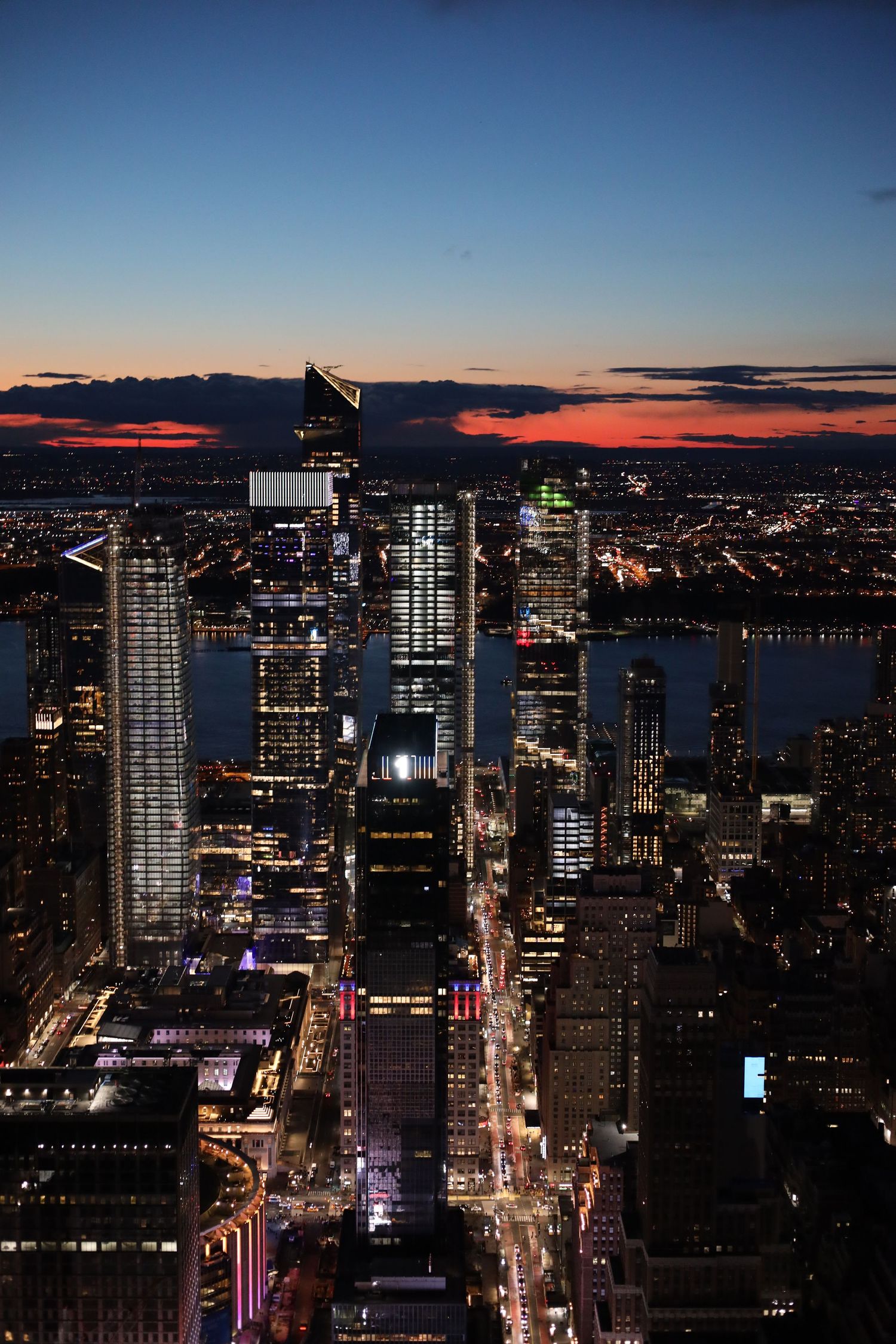 Aerial night view of New York City skyline at sunset with illuminated skyscrapers and glowing streets.