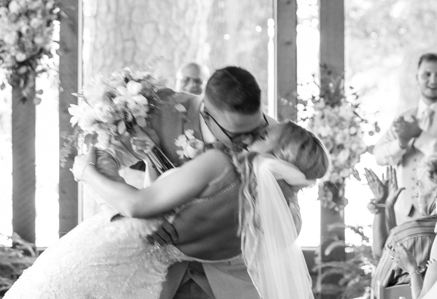 Black and white close-up of bride and groom sharing a passionate first kiss during their wedding ceremony.