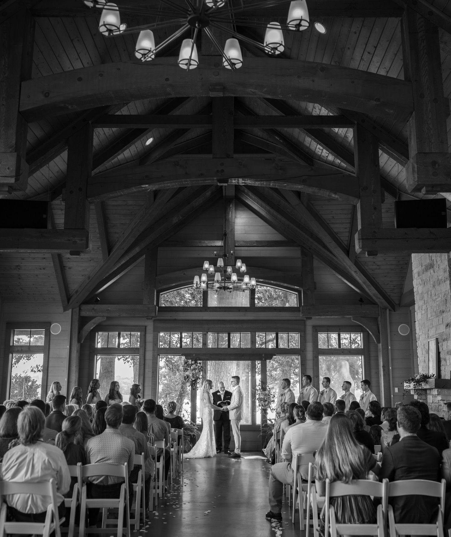 Black and white wedding ceremony inside rustic wooden chapel with vaulted ceiling and chandeliers.