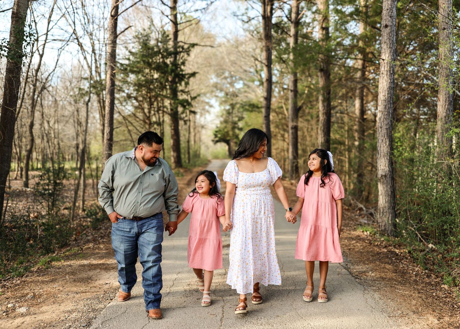 Family of four in pink and white holding hands on path.