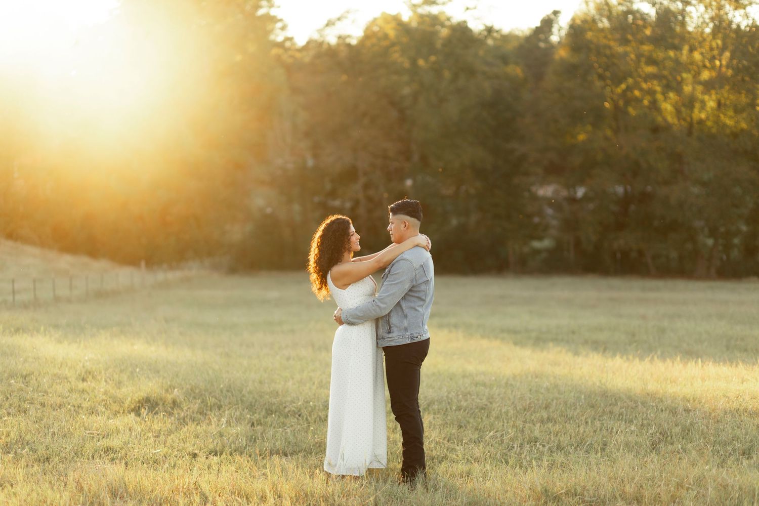 Couple embracing in golden sunset light in a green field.
