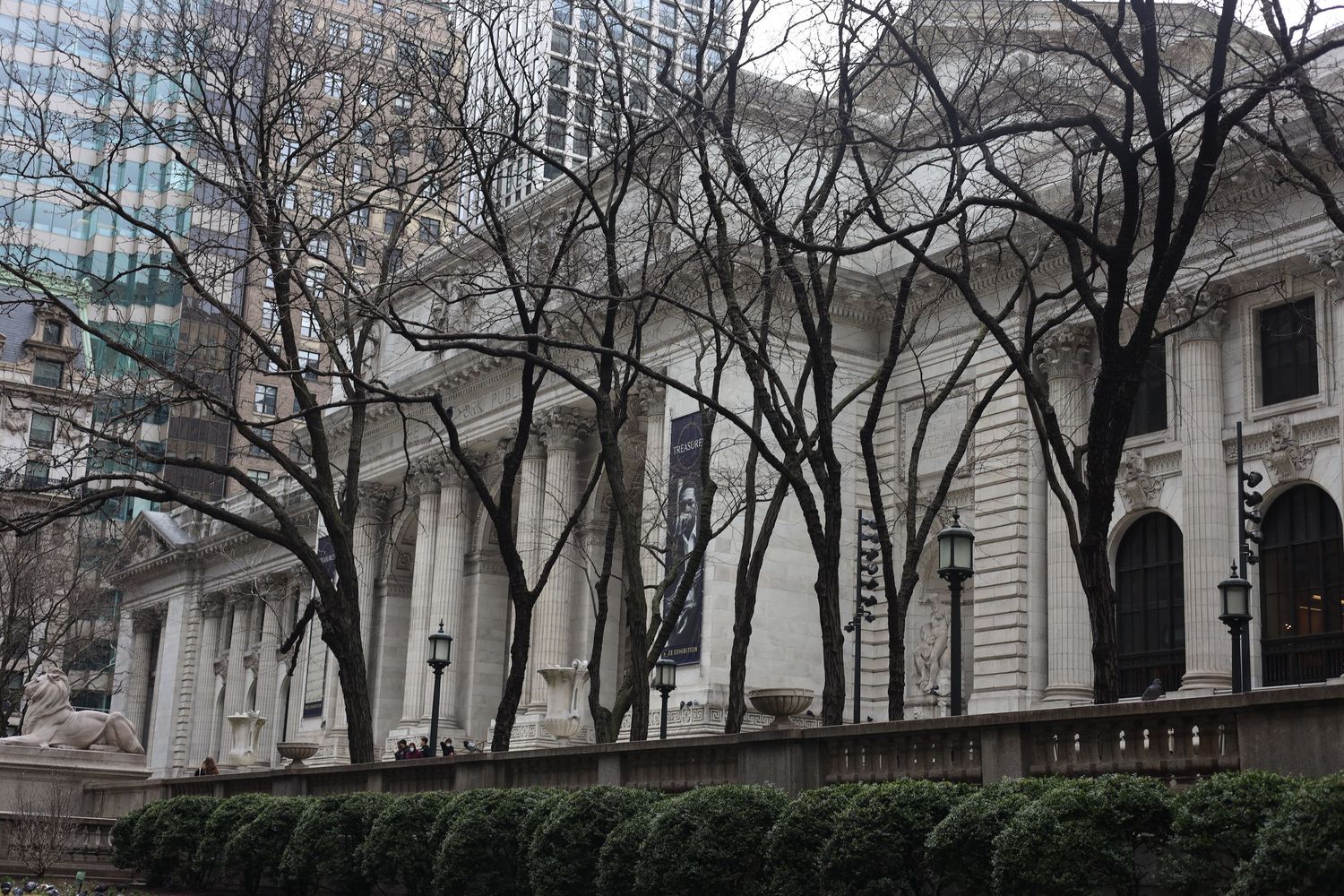 Bare winter trees frame the grand neoclassical facade of the New York Public Library in Midtown Manhattan.