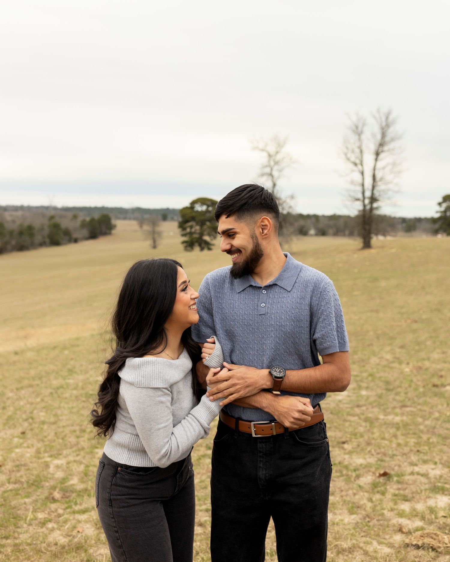 Smiling couple embracing in an open field on a cloudy day.