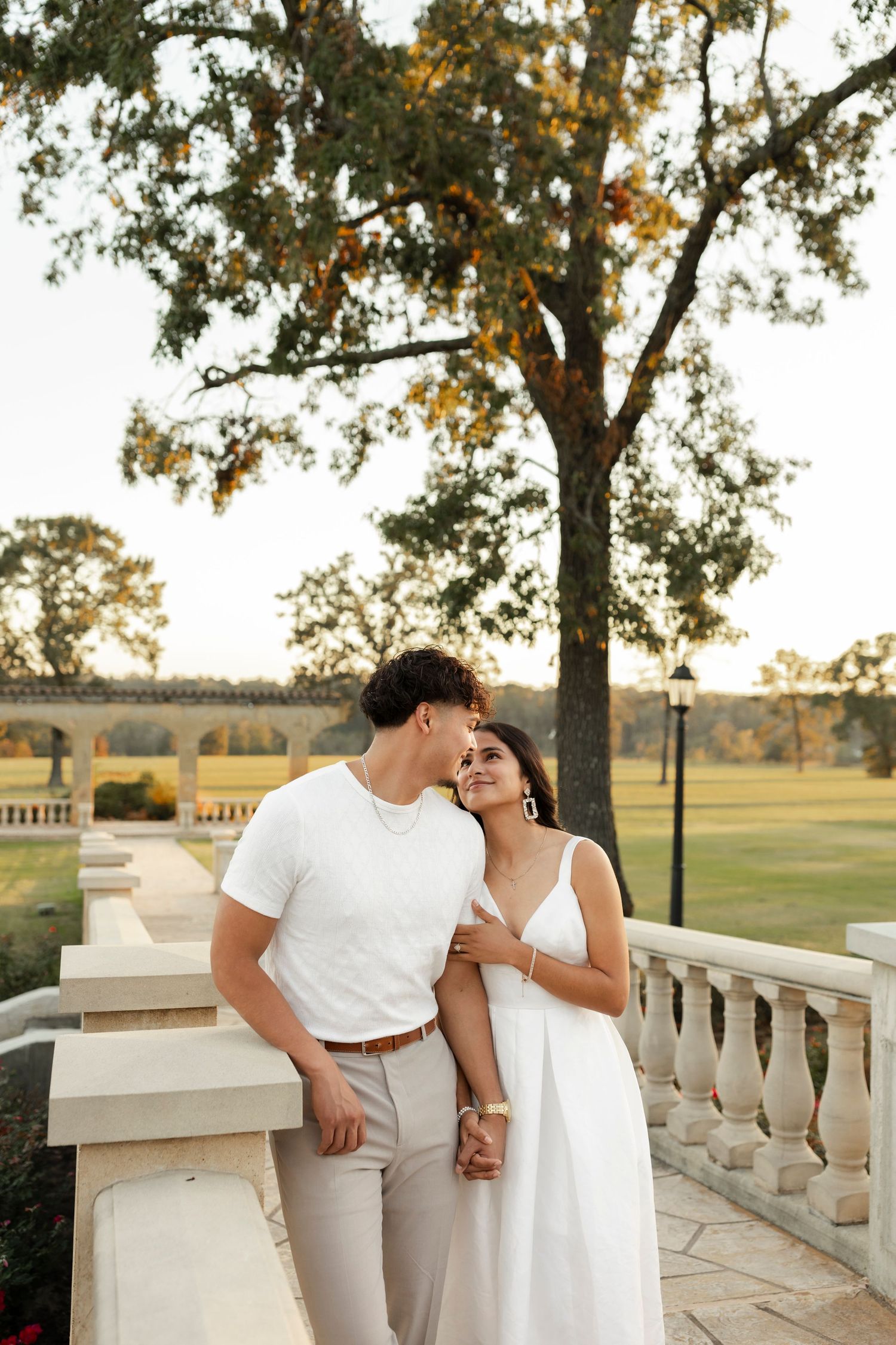 Man kissing woman on cheek near stone balustrade at golden hour.