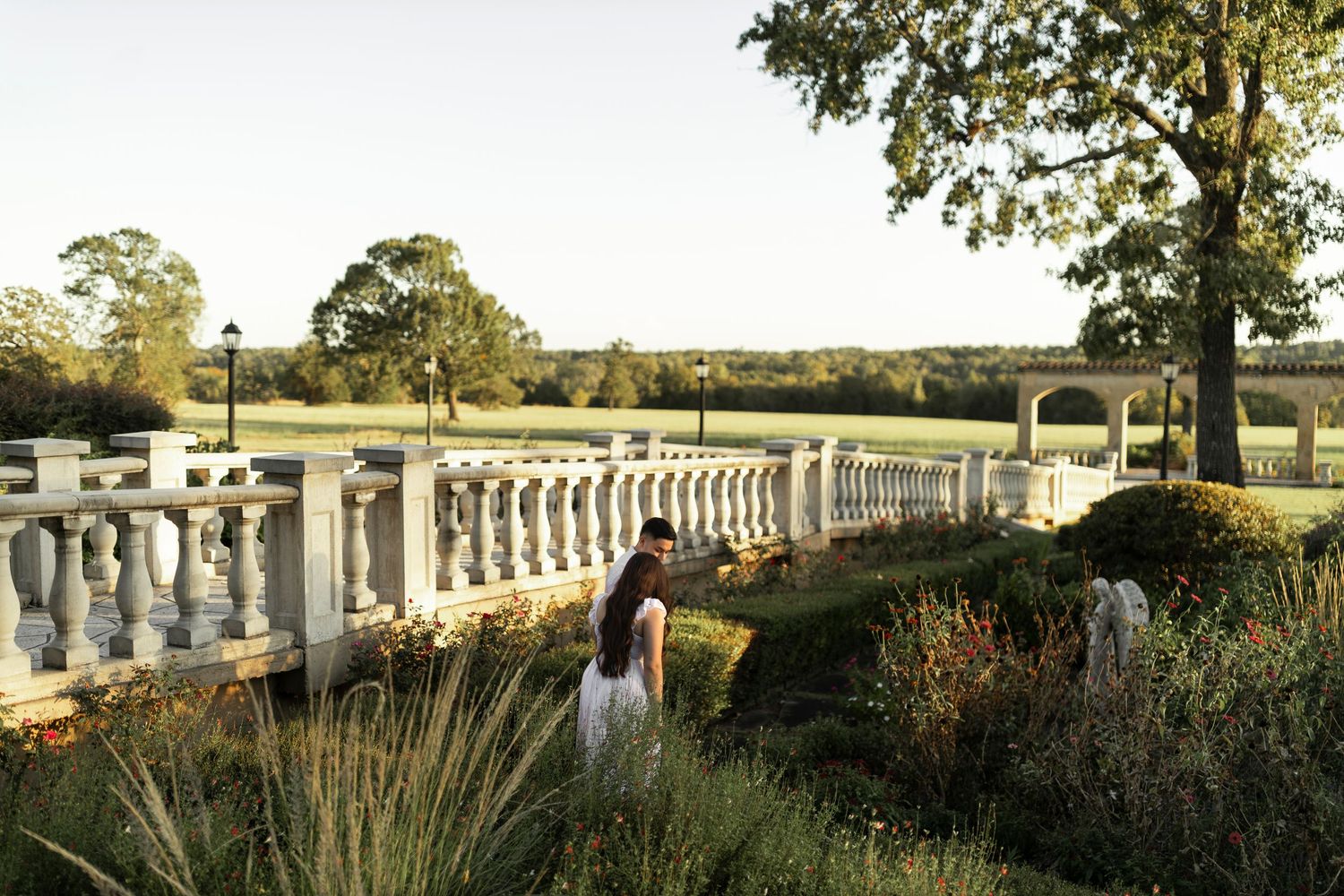 Couple embracing near elegant balustrade at golden hour in garden.
