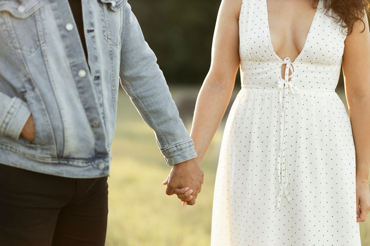 Close-up of couple holding hands, woman in white dress, man in denim jacket.