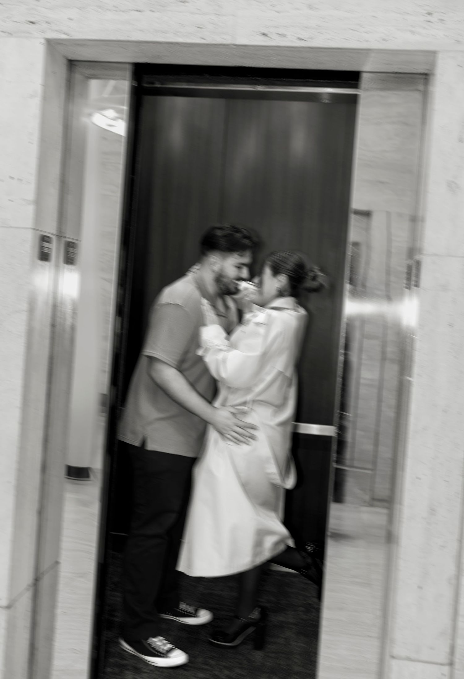 Black and white romantic photo of a couple embracing and kissing inside an elevator with mirrored doors.