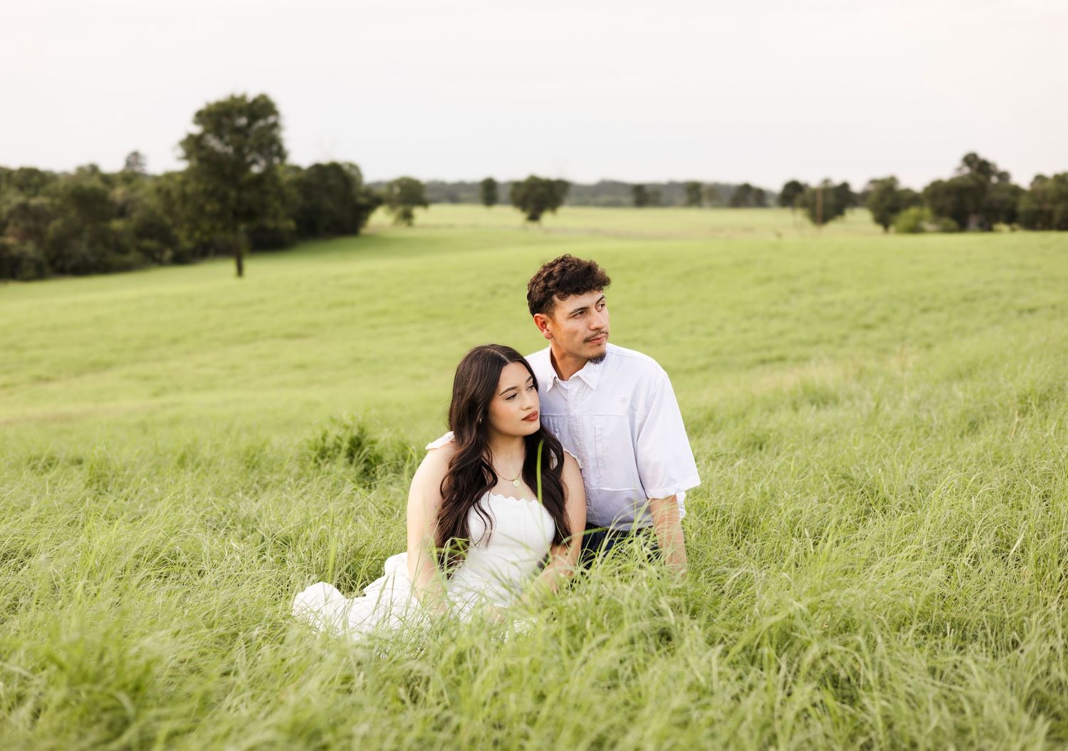 Couple sitting together in a lush green meadow under an overcast sky.