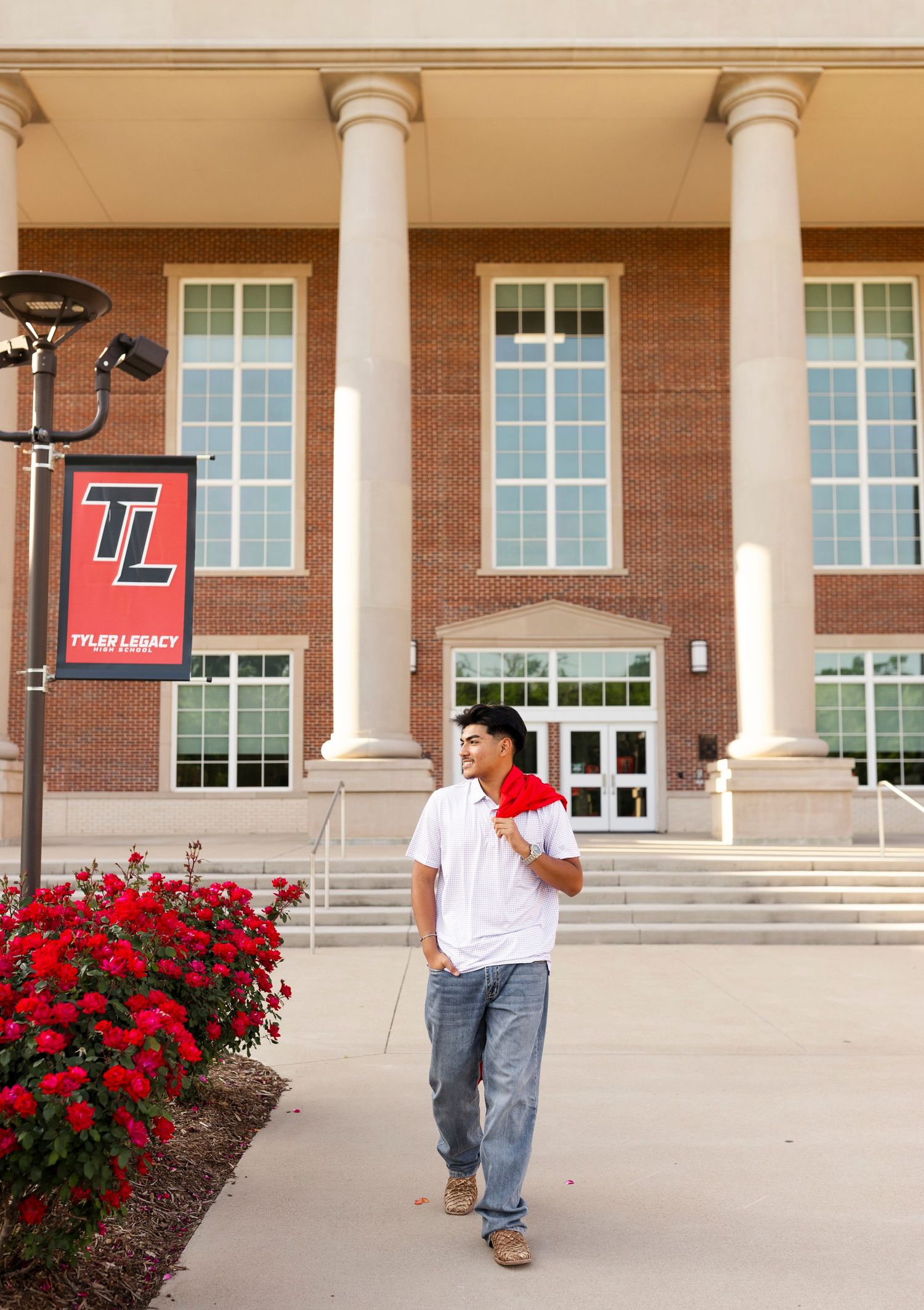 Male student in white shirt holding red graduation cap outside Tyler Legacy High School.