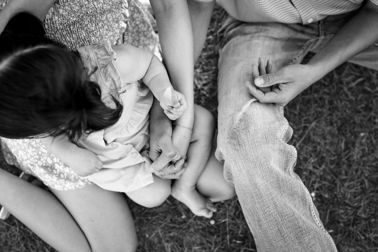 Black and white overhead view of family hands intertwined together while sitting on grass outdoors.
