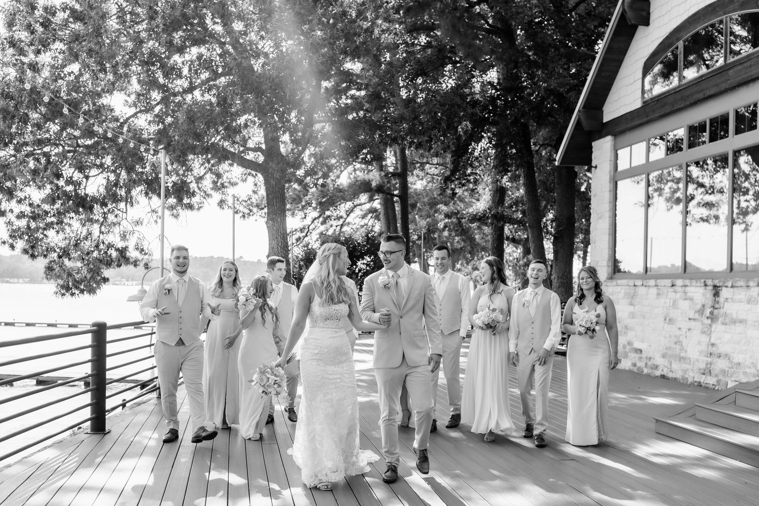 Wedding party walks on a wooden deck surrounded by trees in a classic black and white photo.