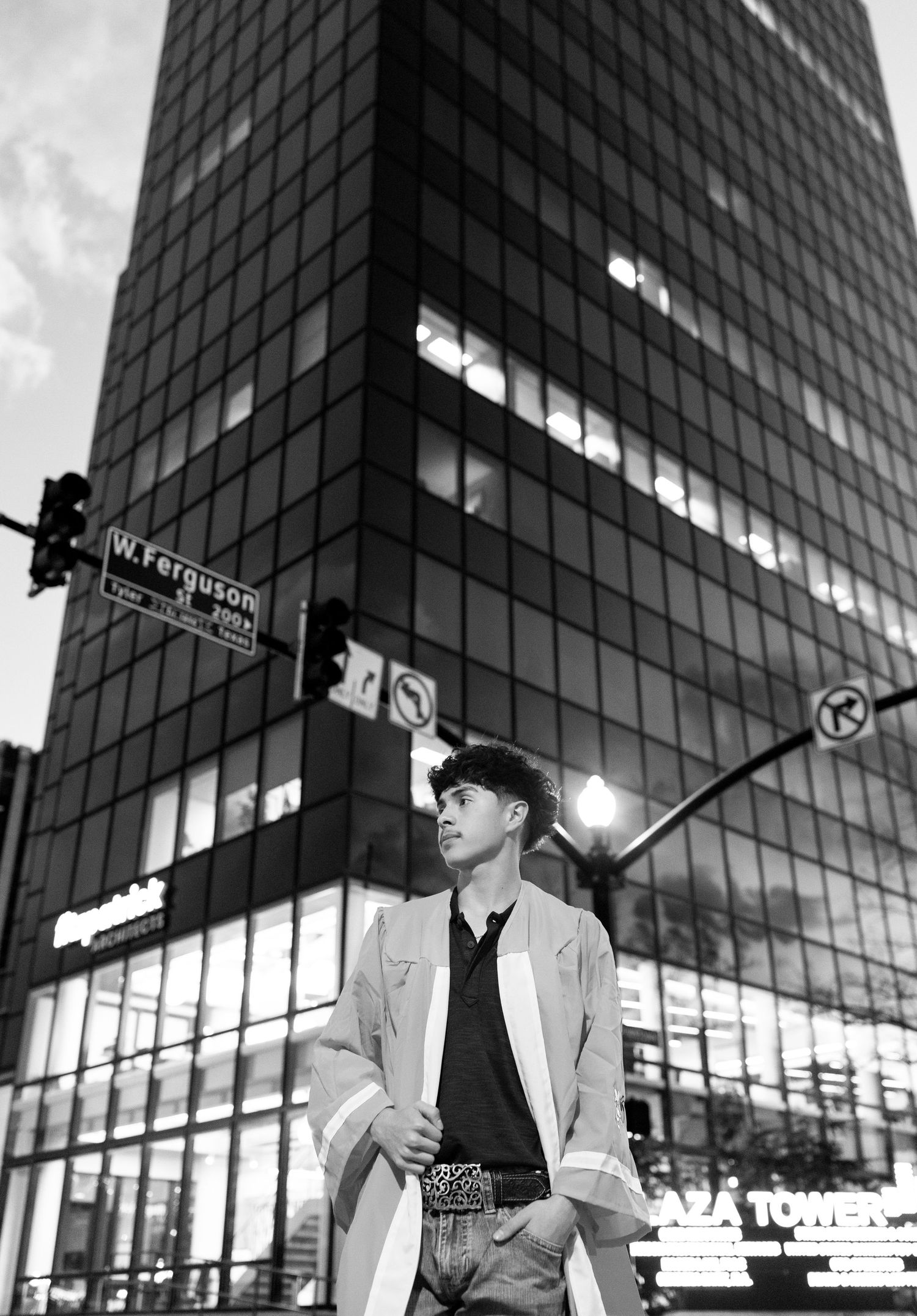 Black and white photo of young man in blazer standing near W. Ferguson street sign at night.
