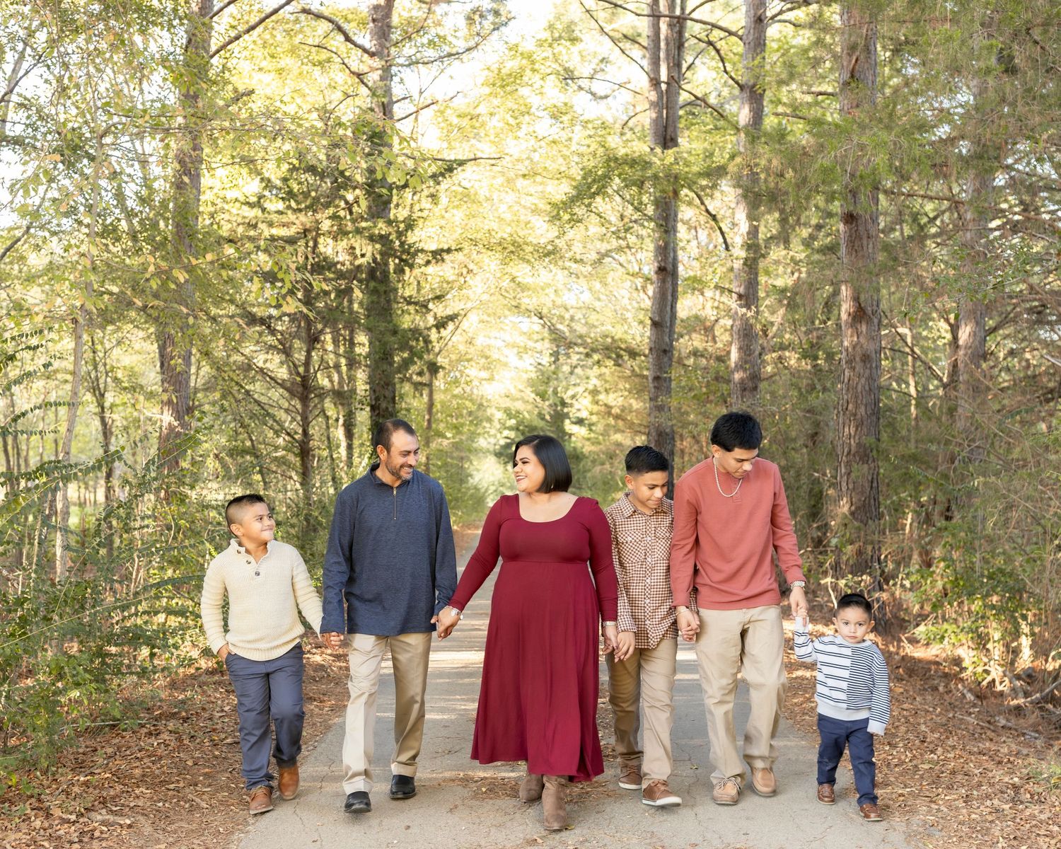 Family of six holding hands walking on a sunlit forest path.