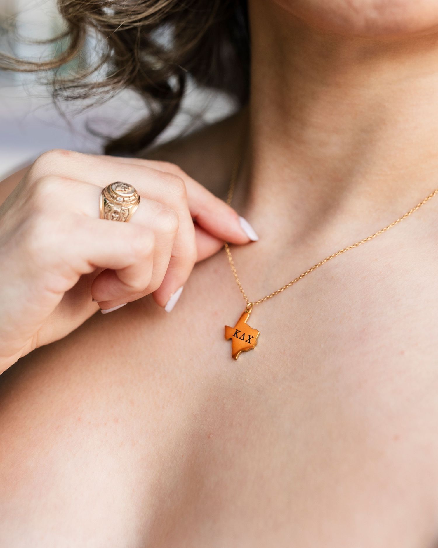 Close-up of gold Texas state pendant necklace and ornate ring worn by a woman in a graduation photo session.