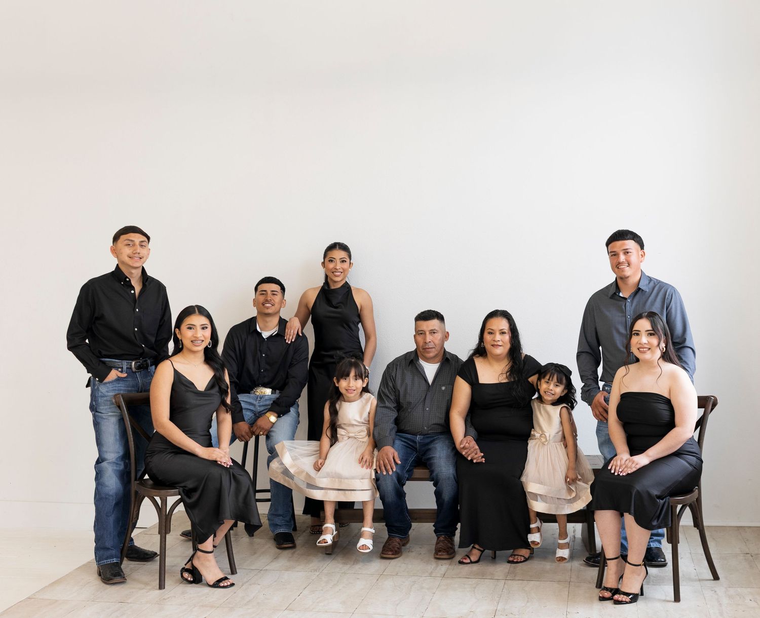 Large family portrait with nine members posed in black outfits against a white background.