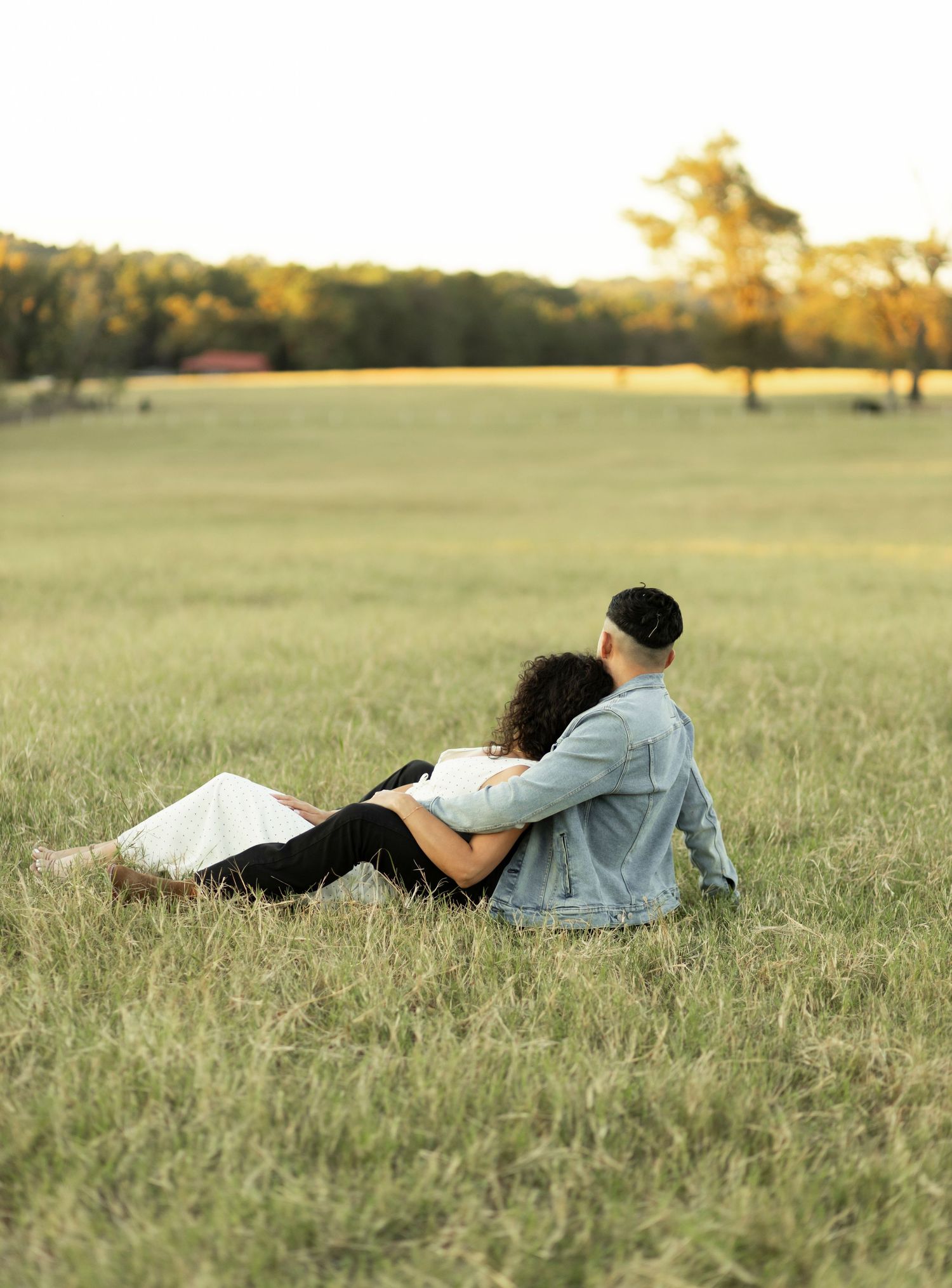 Couple sitting together in an open grassy field enjoying a peaceful golden sunset.