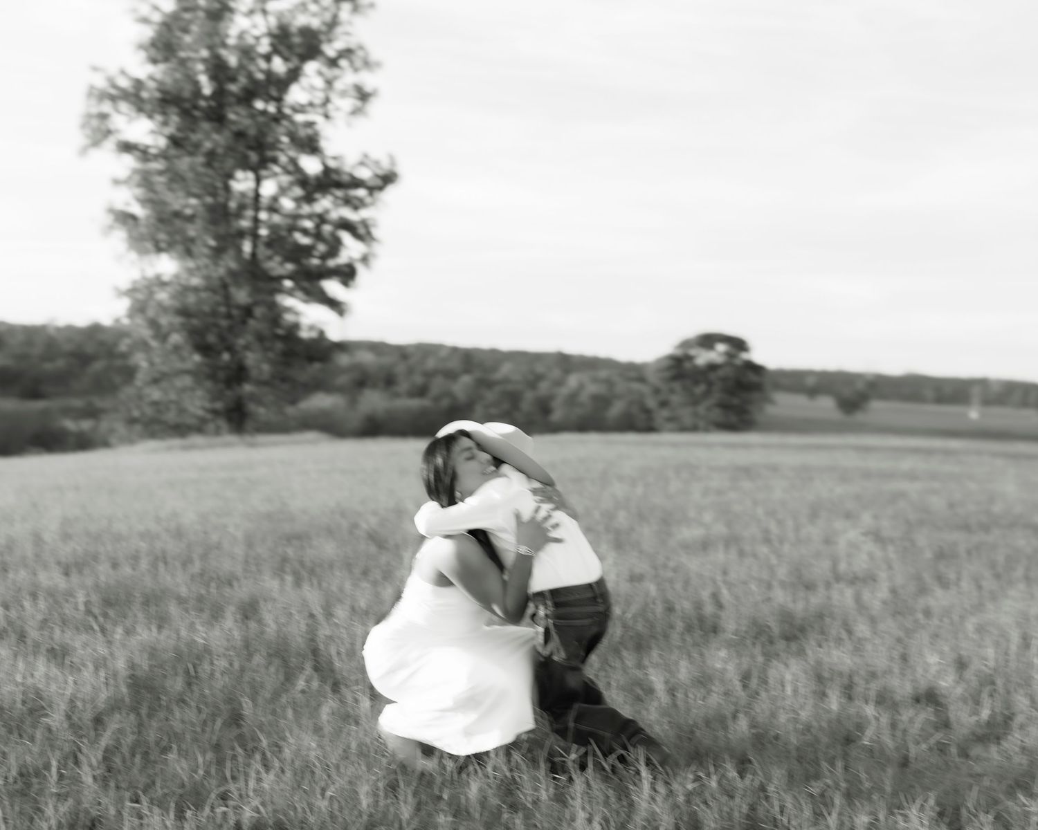 Black and white photo of a woman in a white dress hugging a child in an open field.