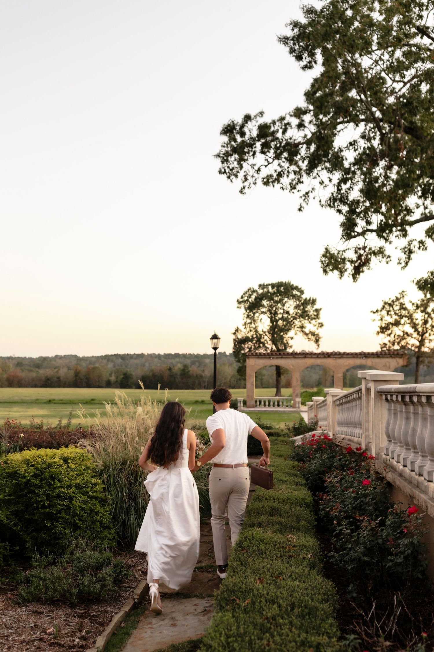 Bride and groom strolling hand-in-hand along elegant garden path at golden hour.