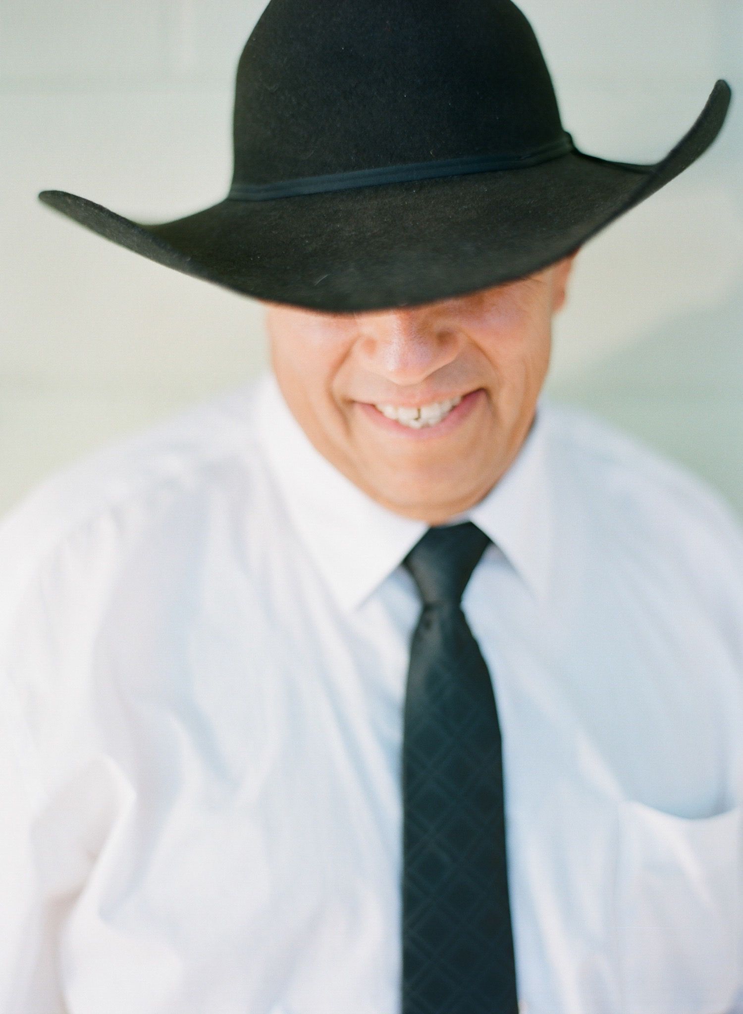 Figure in white shirt and black tie wearing a dark cowboy hat shown in profile.