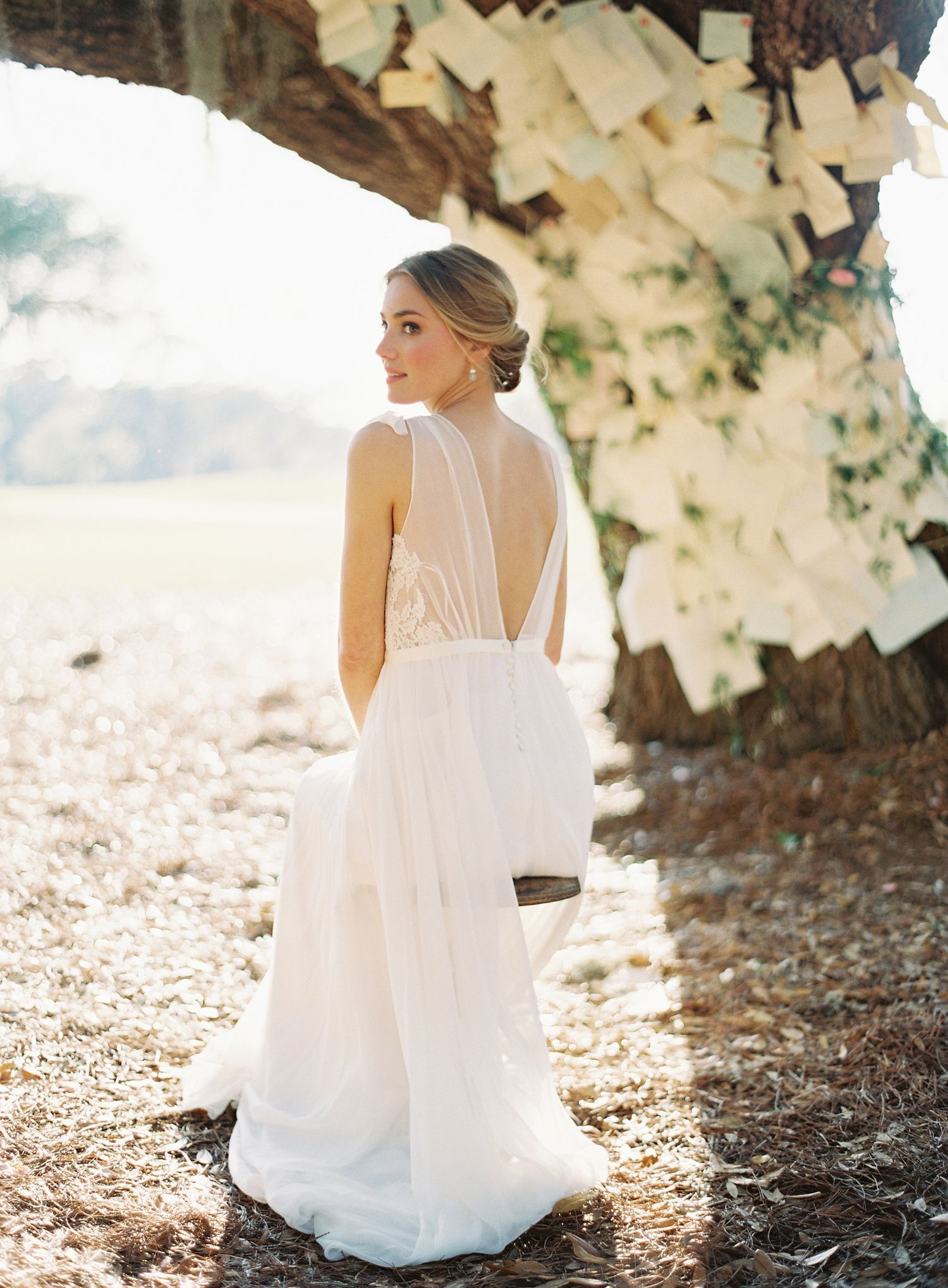 White wedding dress photographed under a tree with hanging paper decorations.
