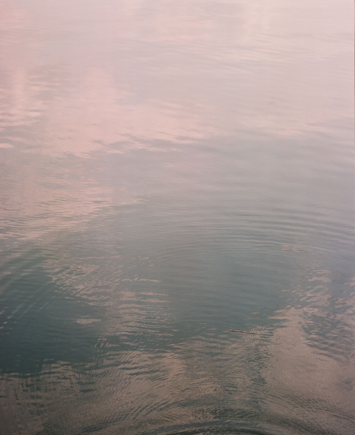 Calm water surface reflecting pink and teal hues during sunset creates a serene rippling pattern.
