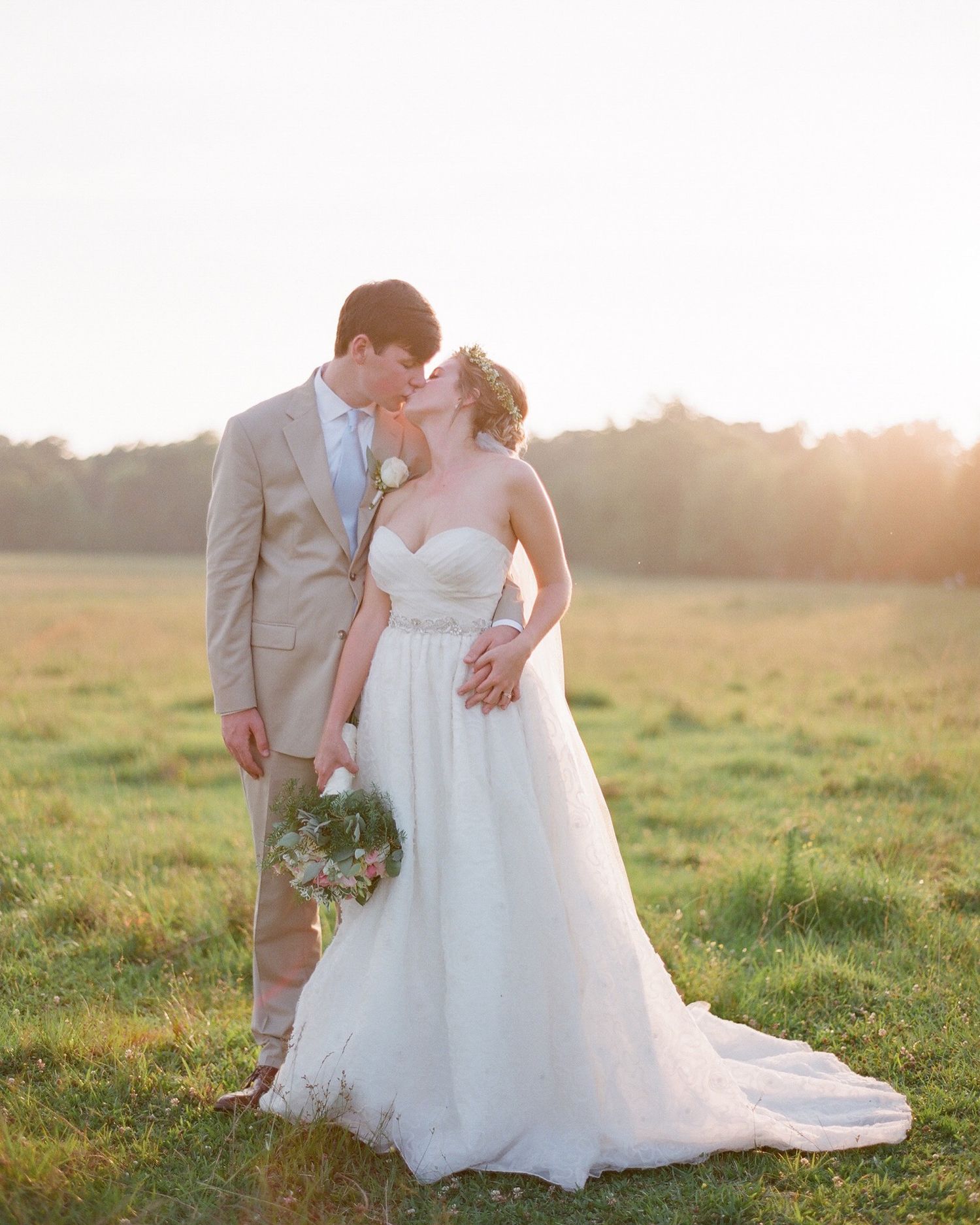 Newlyweds share an intimate moment in a sunlit meadow at golden hour.