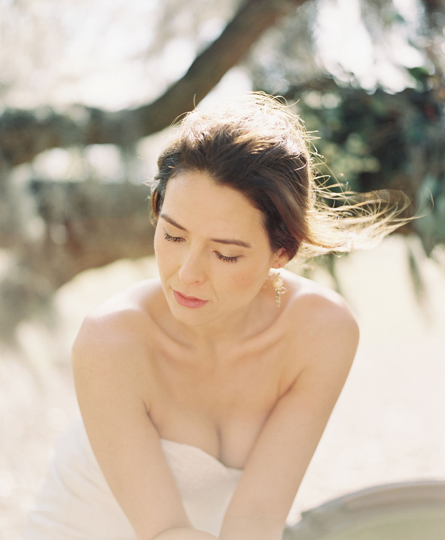 Bride in a strapless white dress poses elegantly in soft natural lighting.