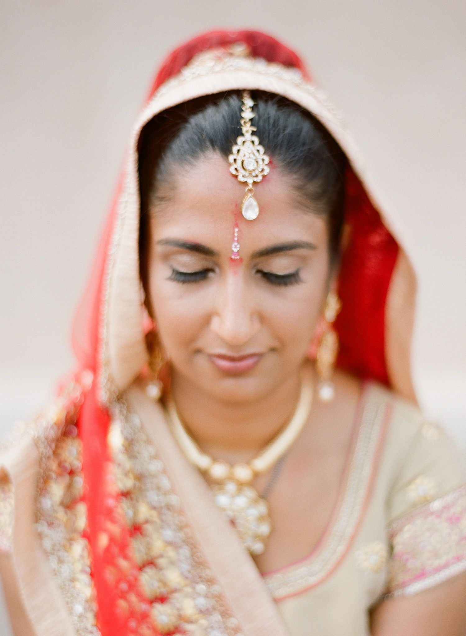 Traditional Indian bride wearing red and gold attire with ornate jewelry and makeup.