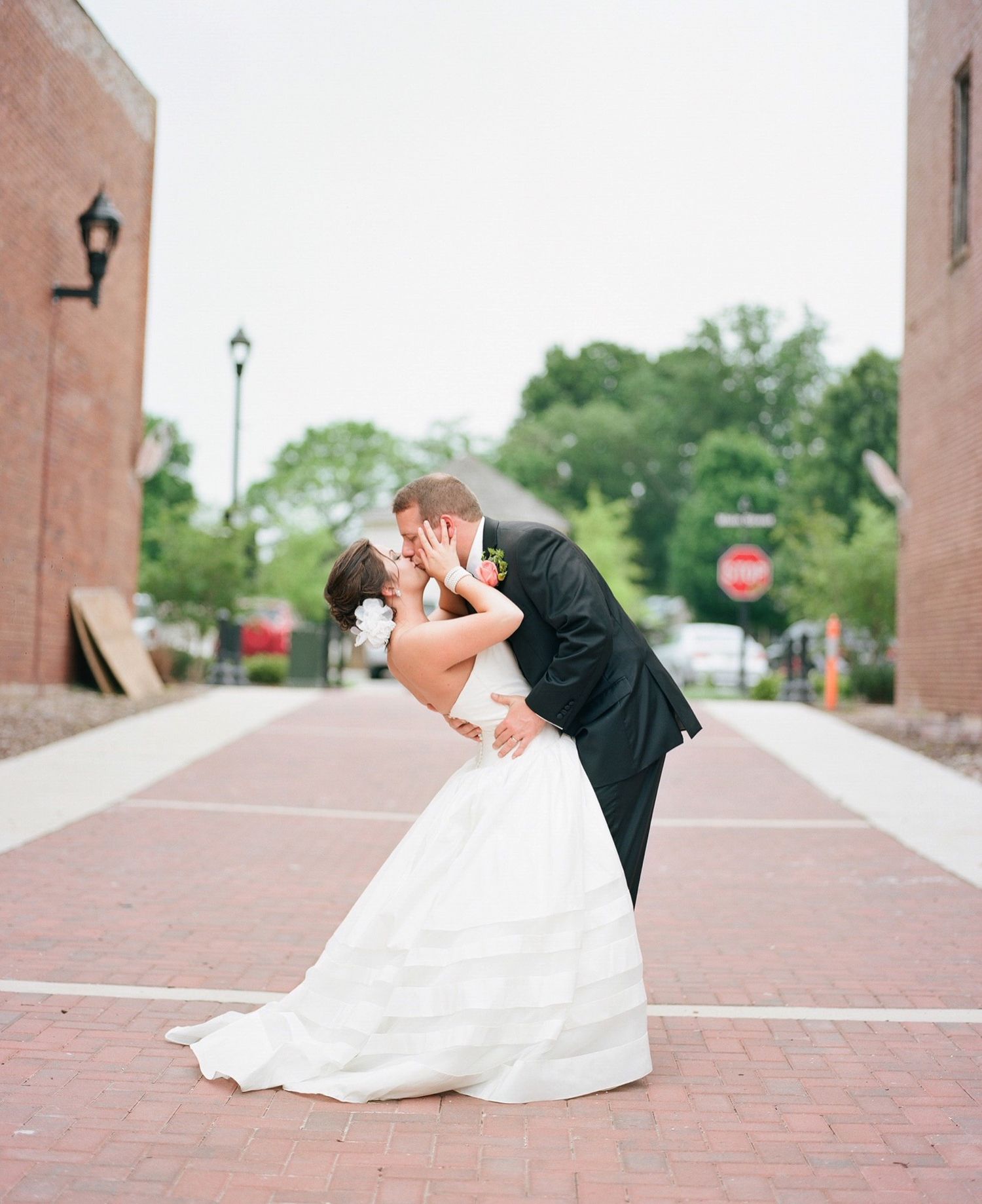 Wedding couple performs dramatic dip pose during outdoor photo session.