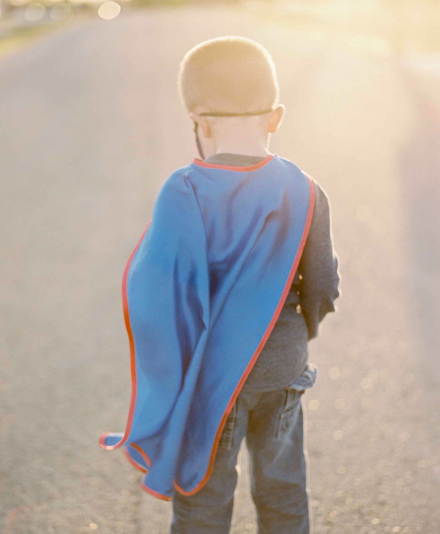 A person wearing a bright blue cape walks away from the camera in golden sunlight.