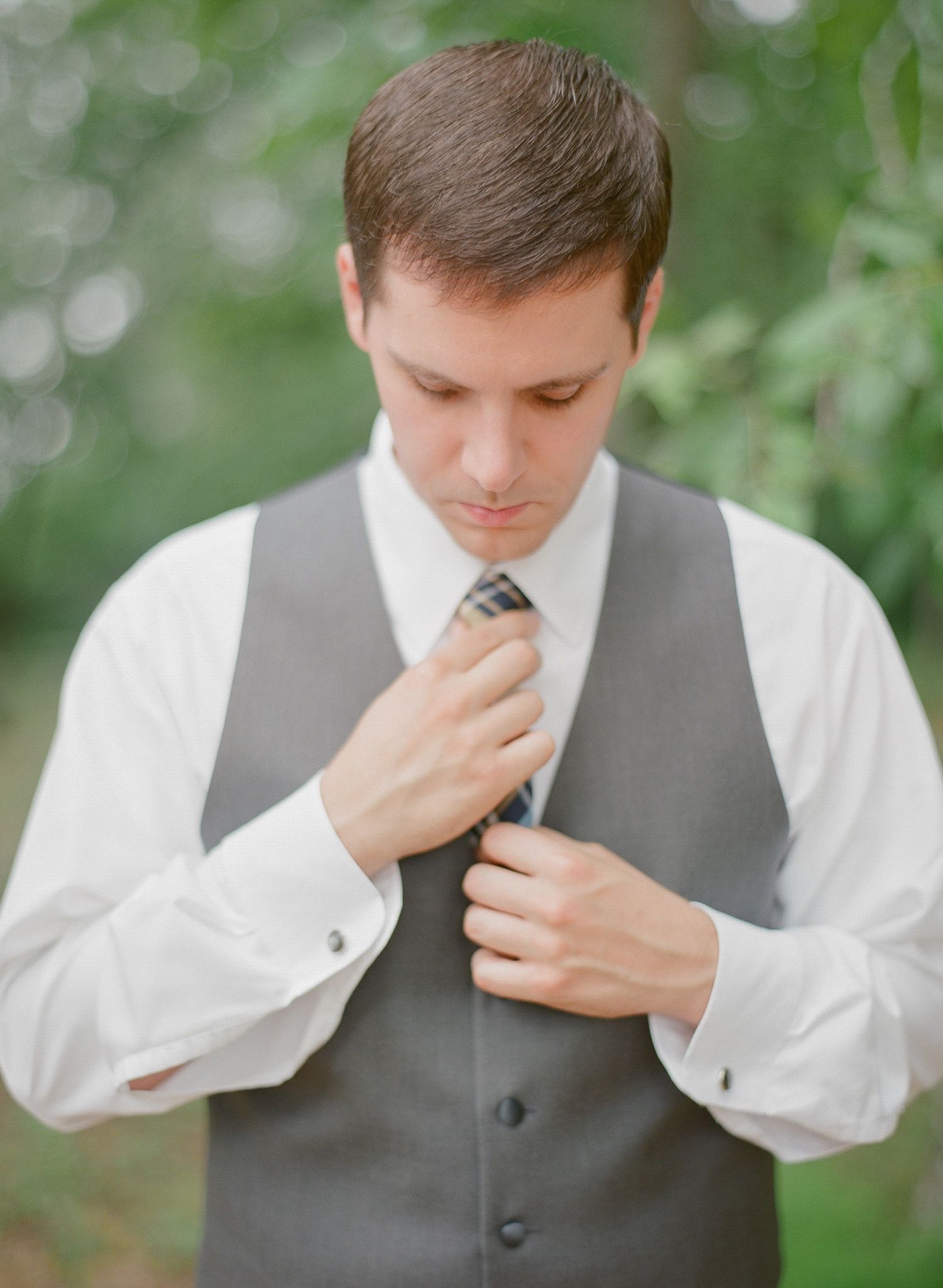 Man in formal vest and tie adjusting his necktie outdoors.