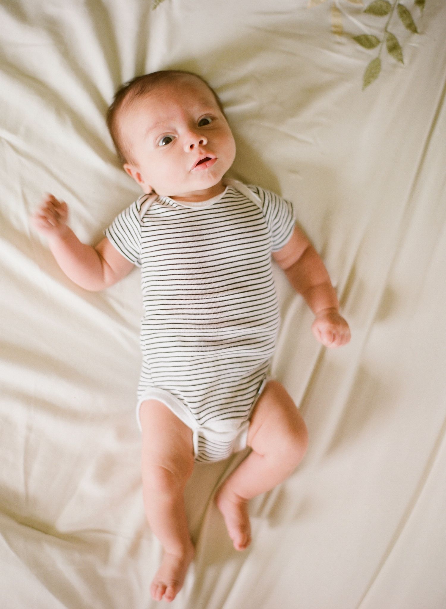 Baby wearing striped onesie lying on white bedding captured from different angles.