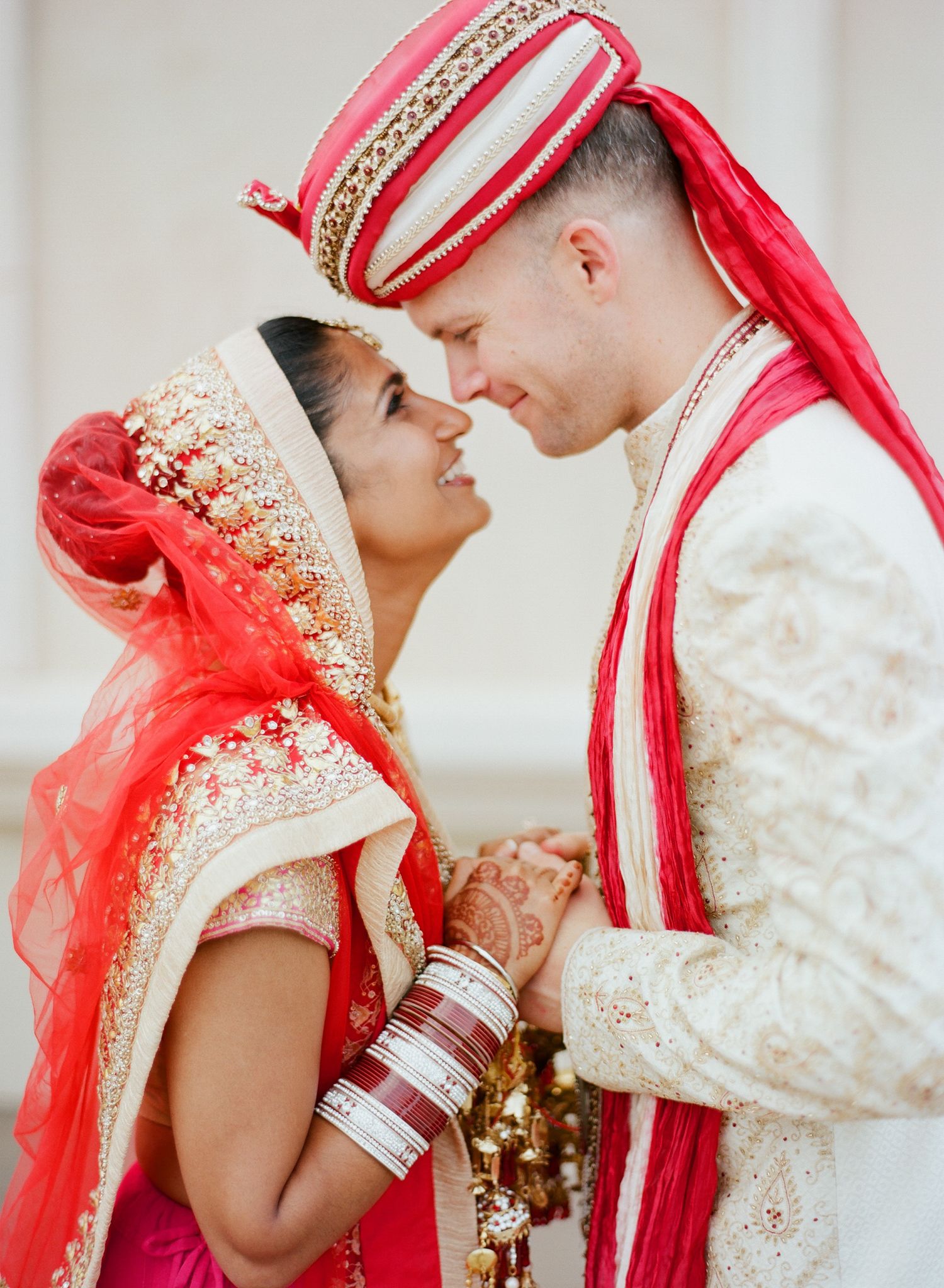 Romantic moment between couple in traditional Indian wedding attire with red and gold details.