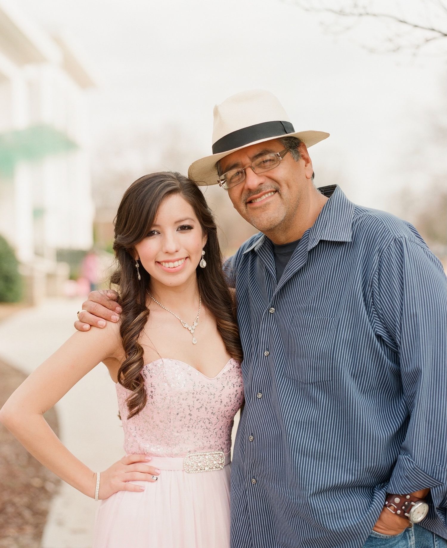Couple posing together outdoors, with one wearing a pink dress and the other in a blue striped shirt.