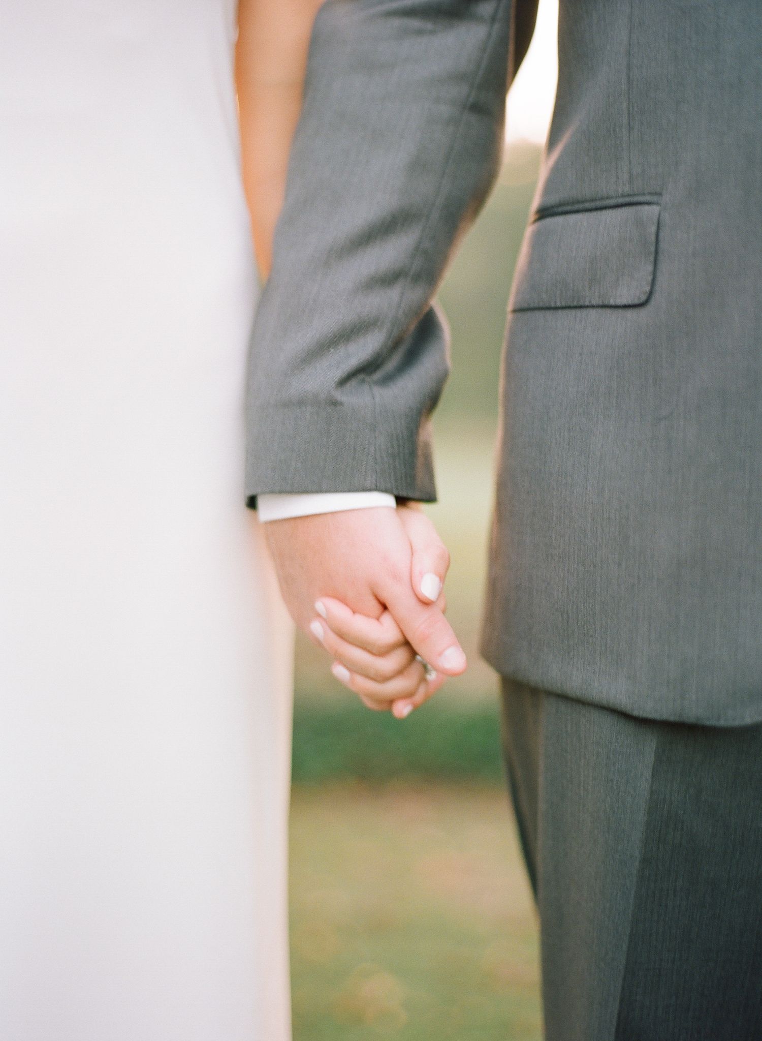 Intimate detail shot of a bride and groom holding hands during their outdoor wedding ceremony.