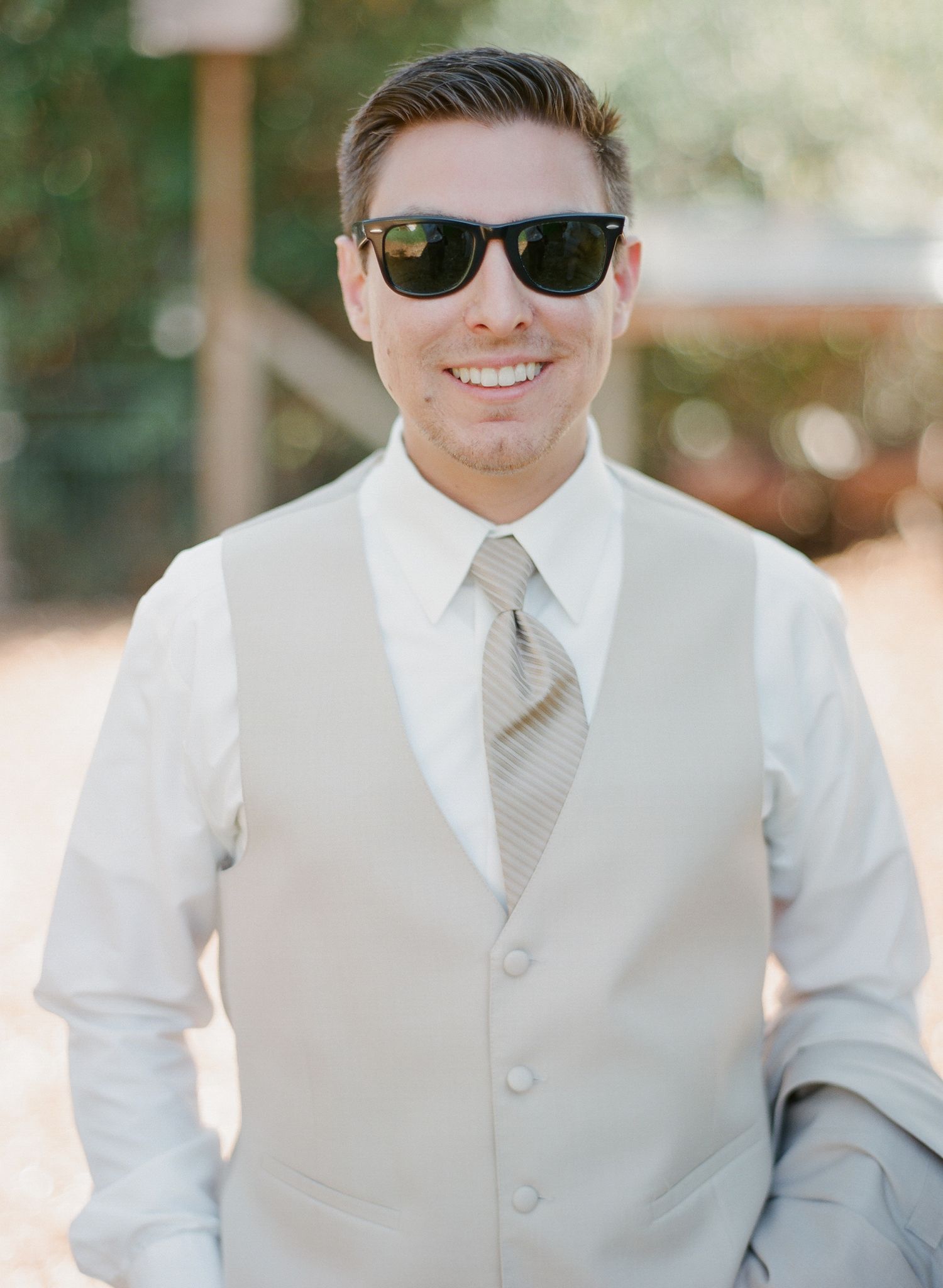 Groom in light gray vest and striped tie wearing sunglasses outdoors.