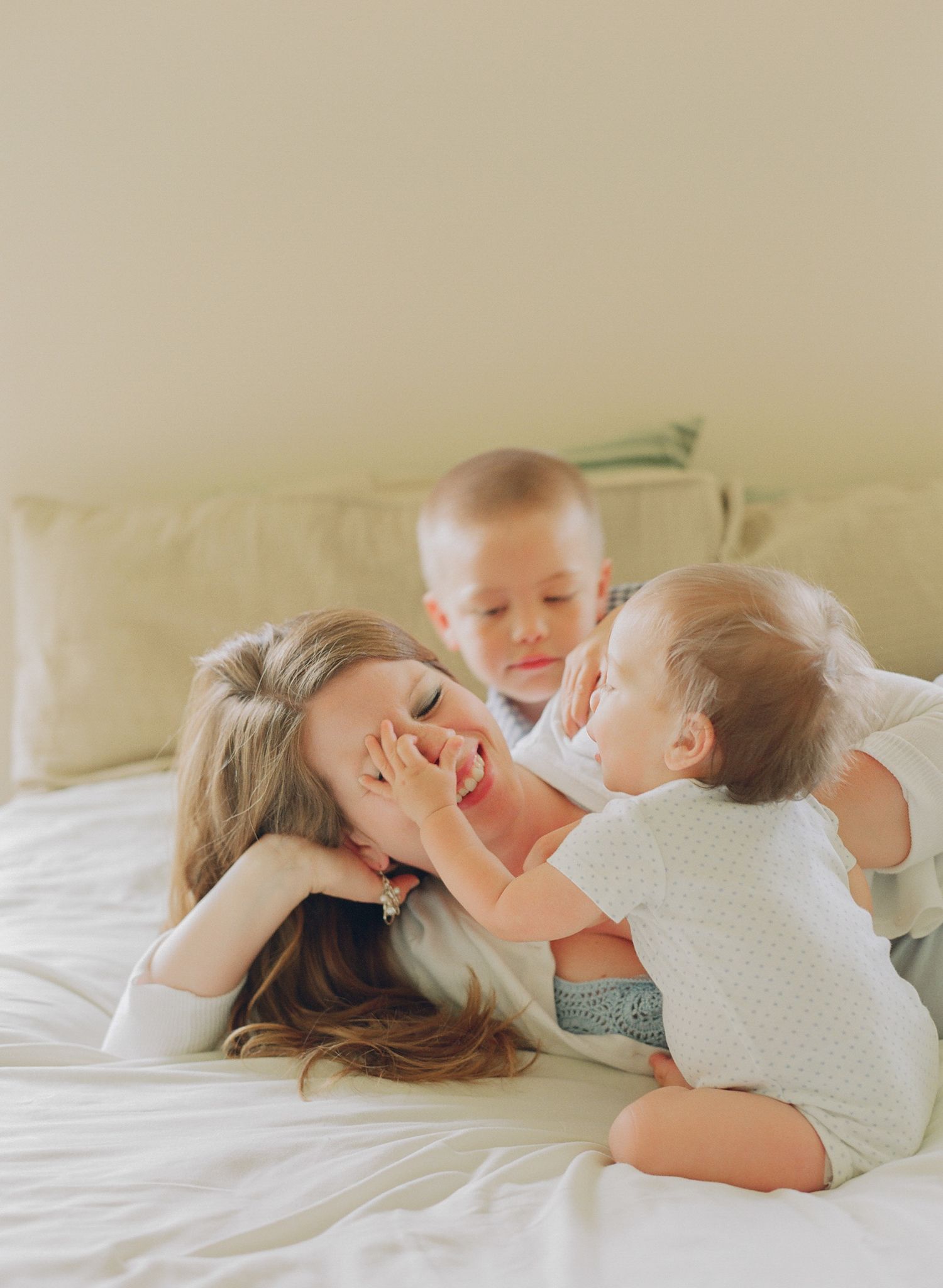 Tender family moment captured on white bedding in soft natural lighting.