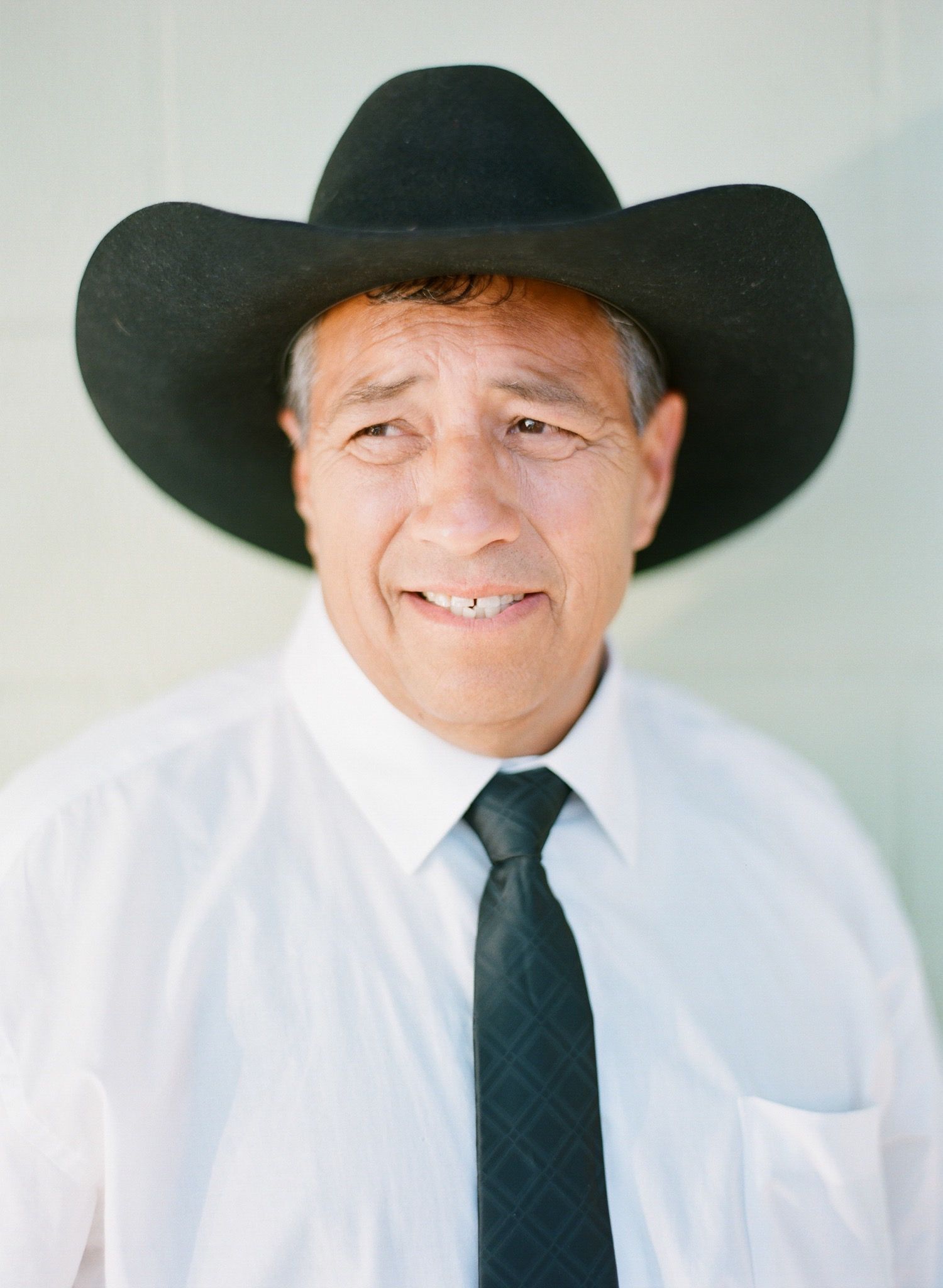 Person in white dress shirt and black tie smiling while wearing a black cowboy hat.