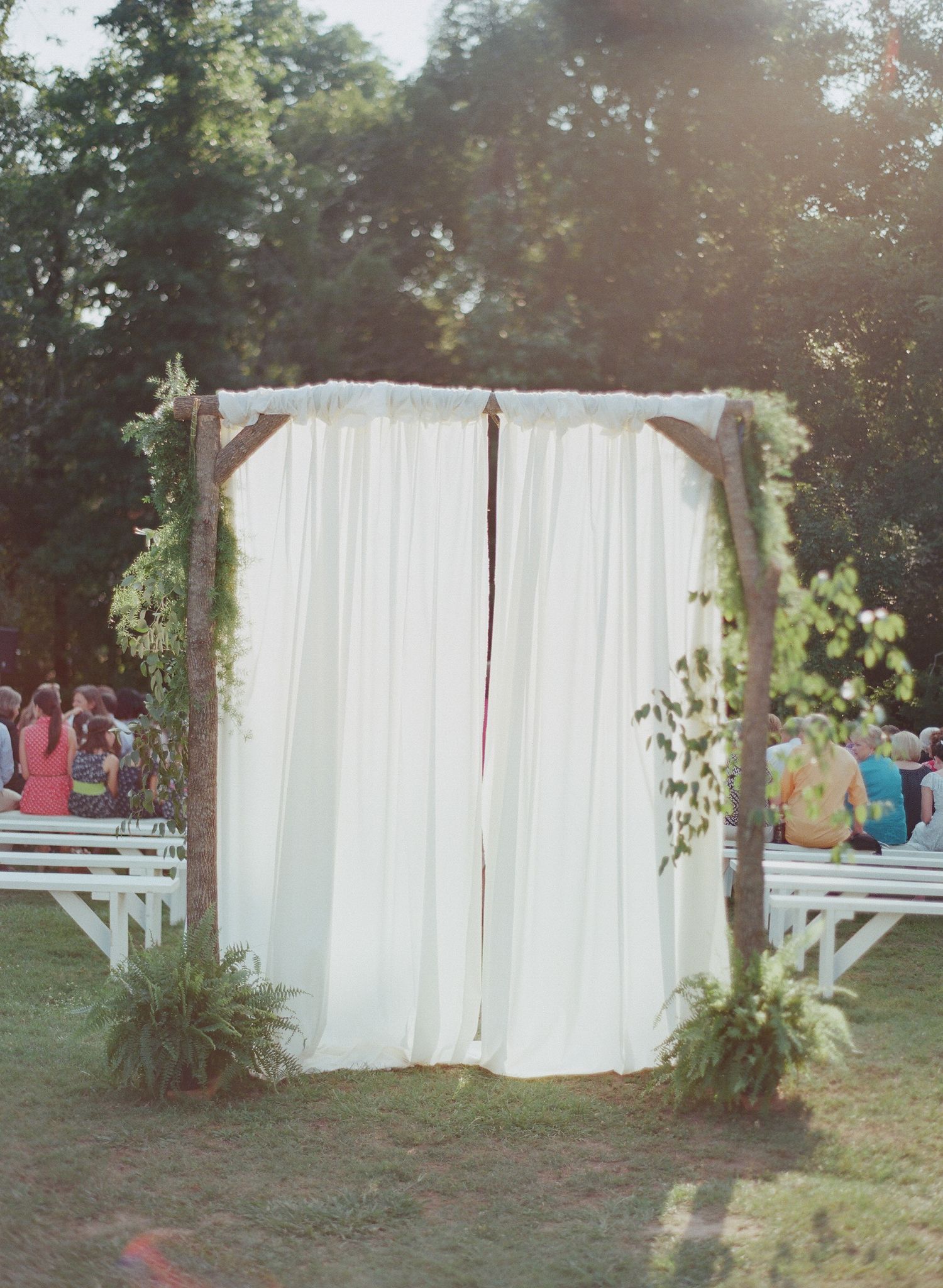 White curtains hanging outdoors between trees create an elegant outdoor space for a garden event.